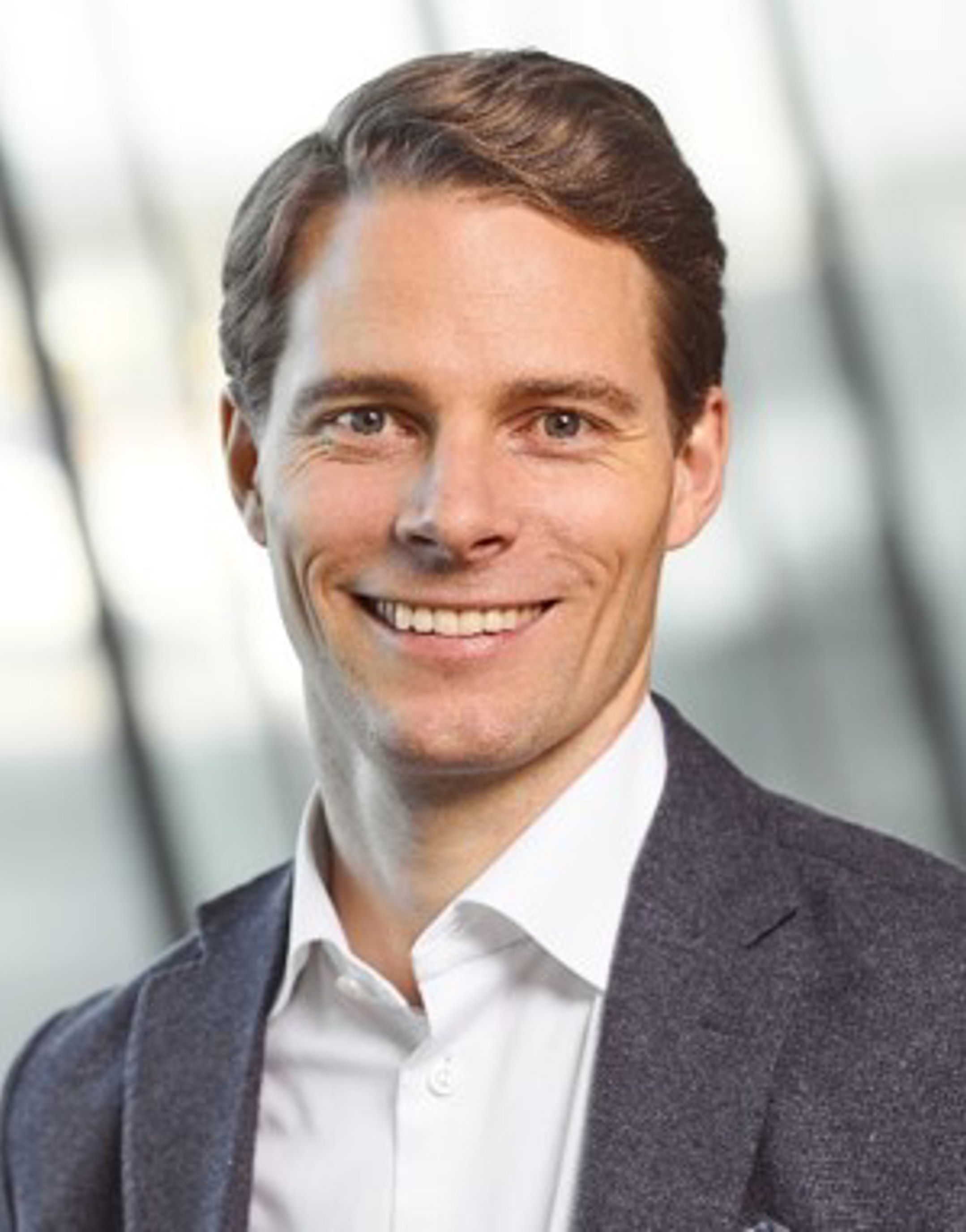 Smilende profesjonell mann i dress, stående mot en uskarp kontorbakgrunn