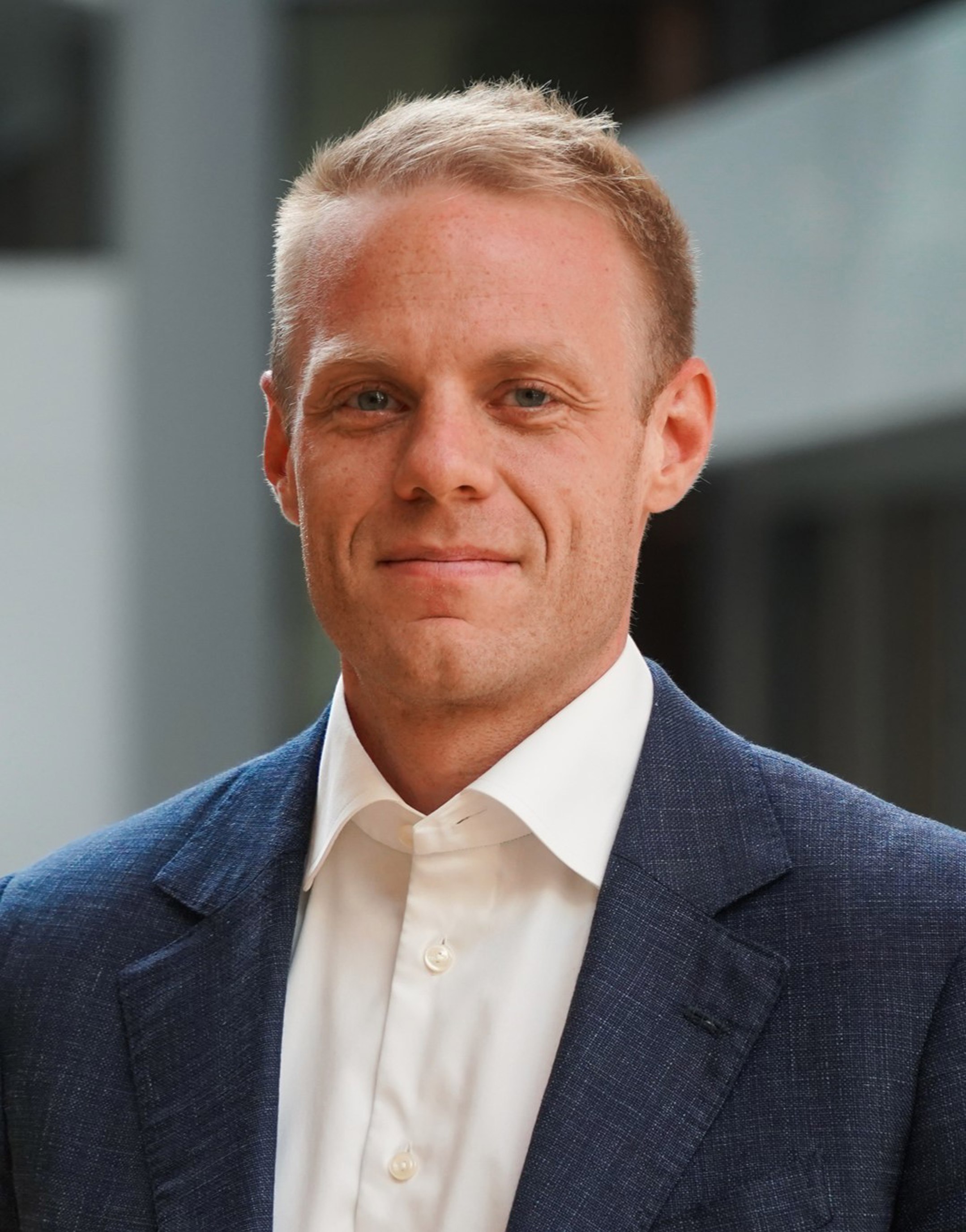 Profesjonell mann i blå dress og hvit skjorte, står innendørs med uskarp bakgrunn