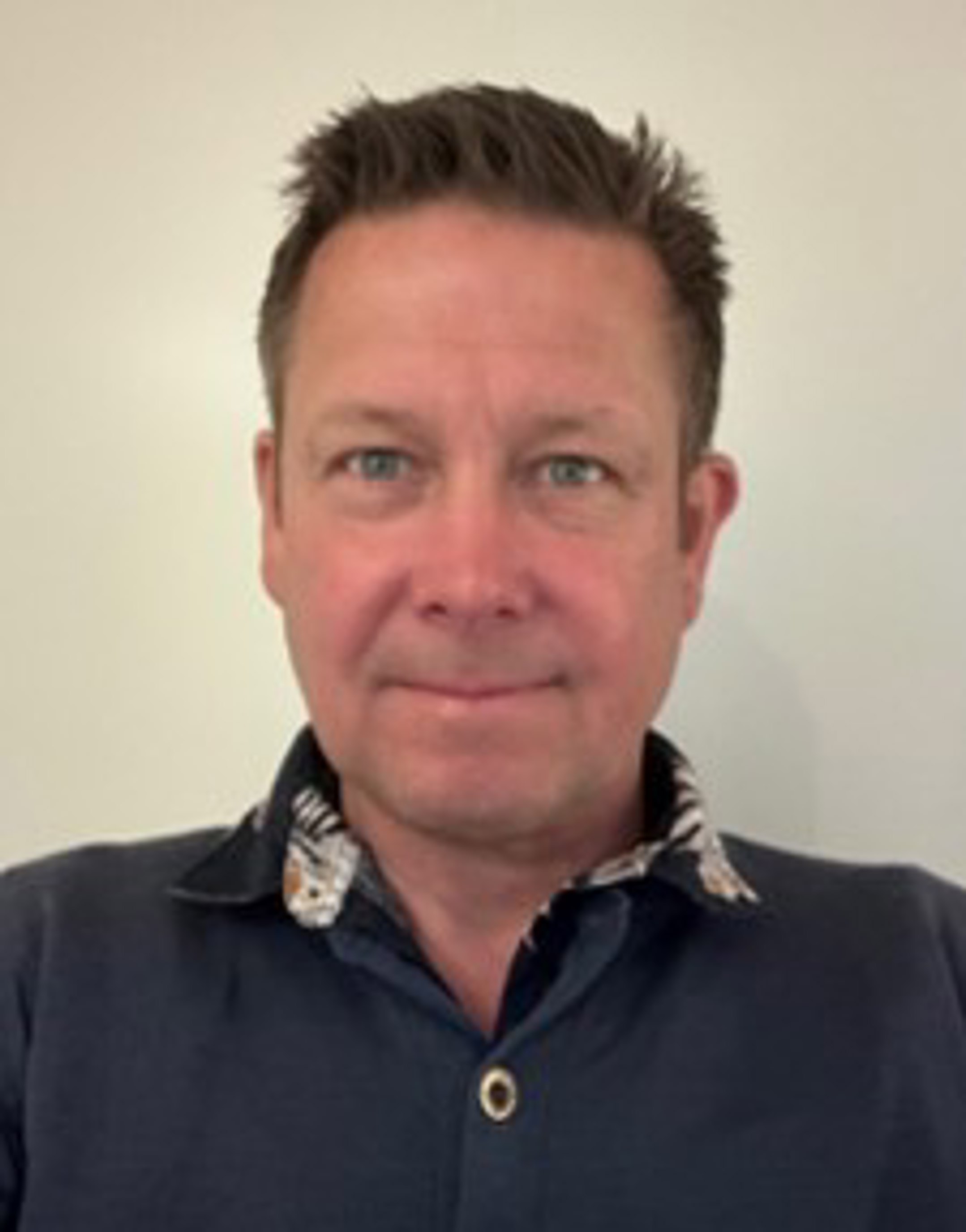 Mann i blå skjorte foran hvit bakgrunn, ser rett mot kameraet