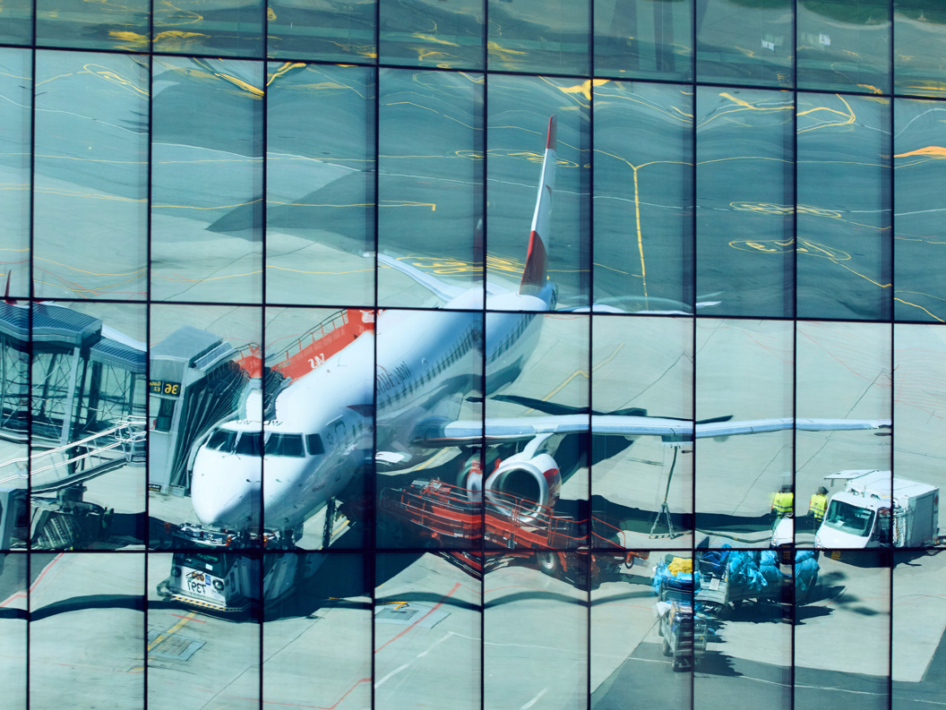 Reflection of a commercial airplane at an airport gate, captured on a glass building facade