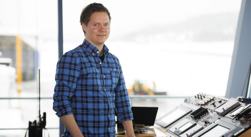 Ein person i blå rutete skjorte står ved eit kontrollbord med skjermar og utstyr, med utsikt over ein snødekt bakgrunn.