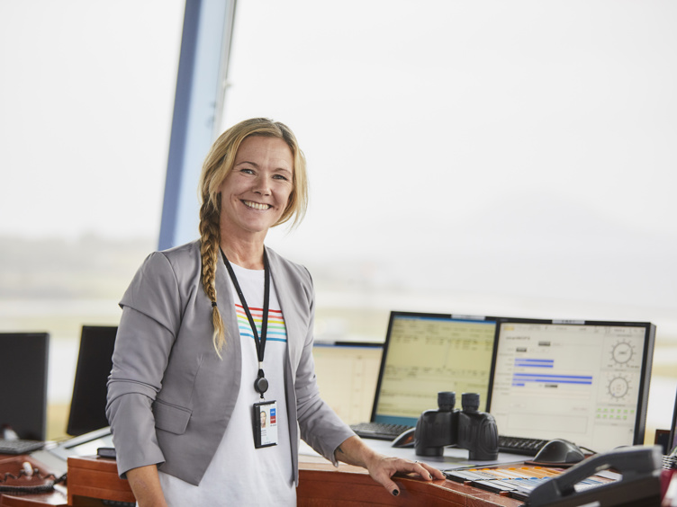 Kvinne i uniform smiler på broen av et skip, omringet av skjermer og navigasjonsutstyr.