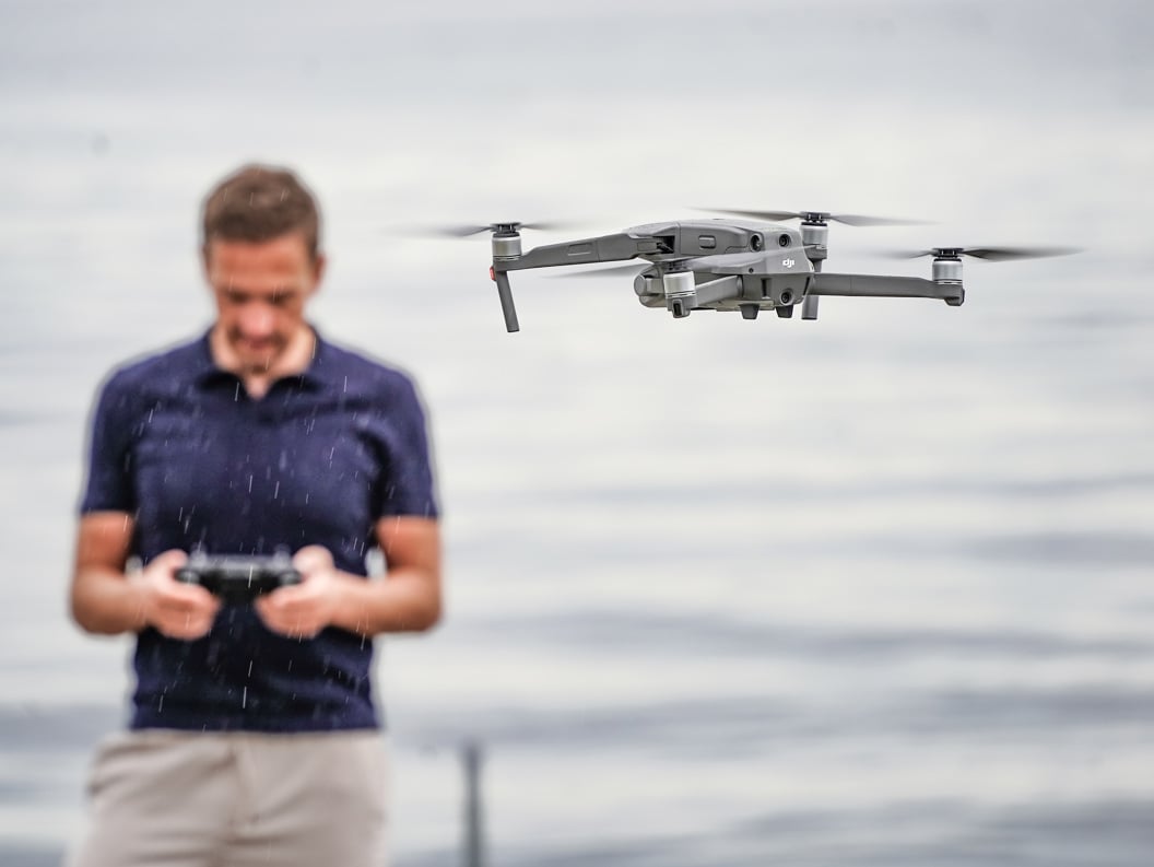 Mann styrer drone med fjernkontroll ved vannkanten