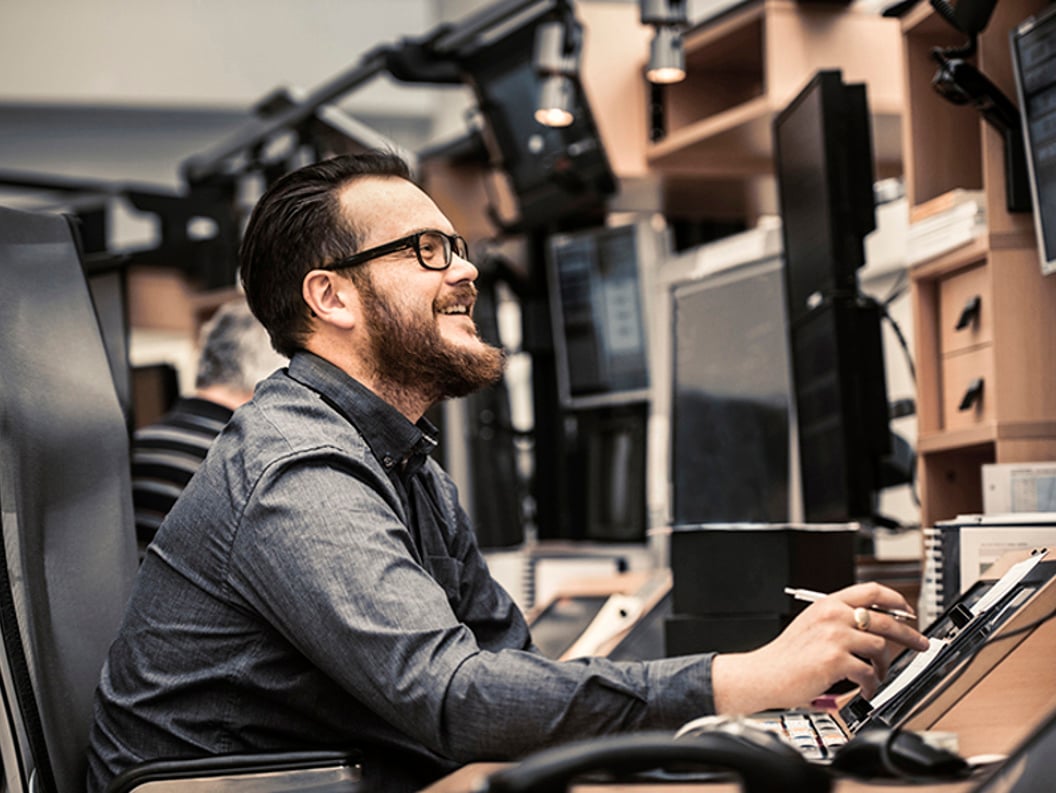 Smilende mann som jobber ved et skrivebord med flere dataskjermer, bruker en digital penn, i et moderne kontormiljø