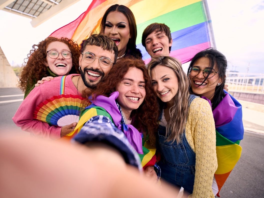 Gruppe av glade mennesker som feirer med regnbueflagg, et symbol på LGBTQ+-stolthet, utendørs på en solfylt dag