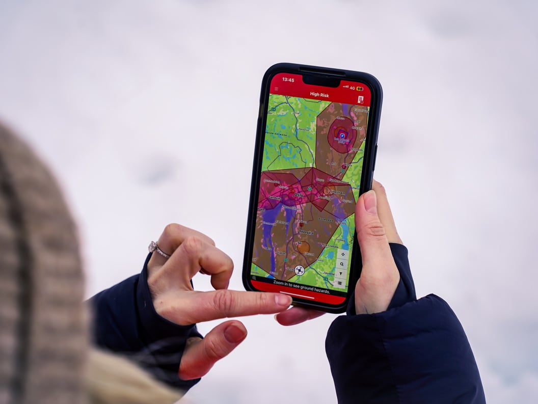 Person som bruker ein smarttelefon med kartapplikasjon som viser risikoområde i Oslo-regionen, vinterdag