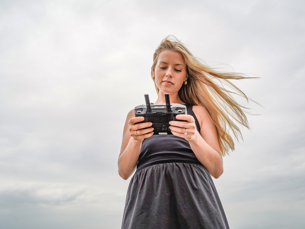Kvinne styrer drone med fjernkontroll, vind blåser i håret hennes under en overskyet himmel