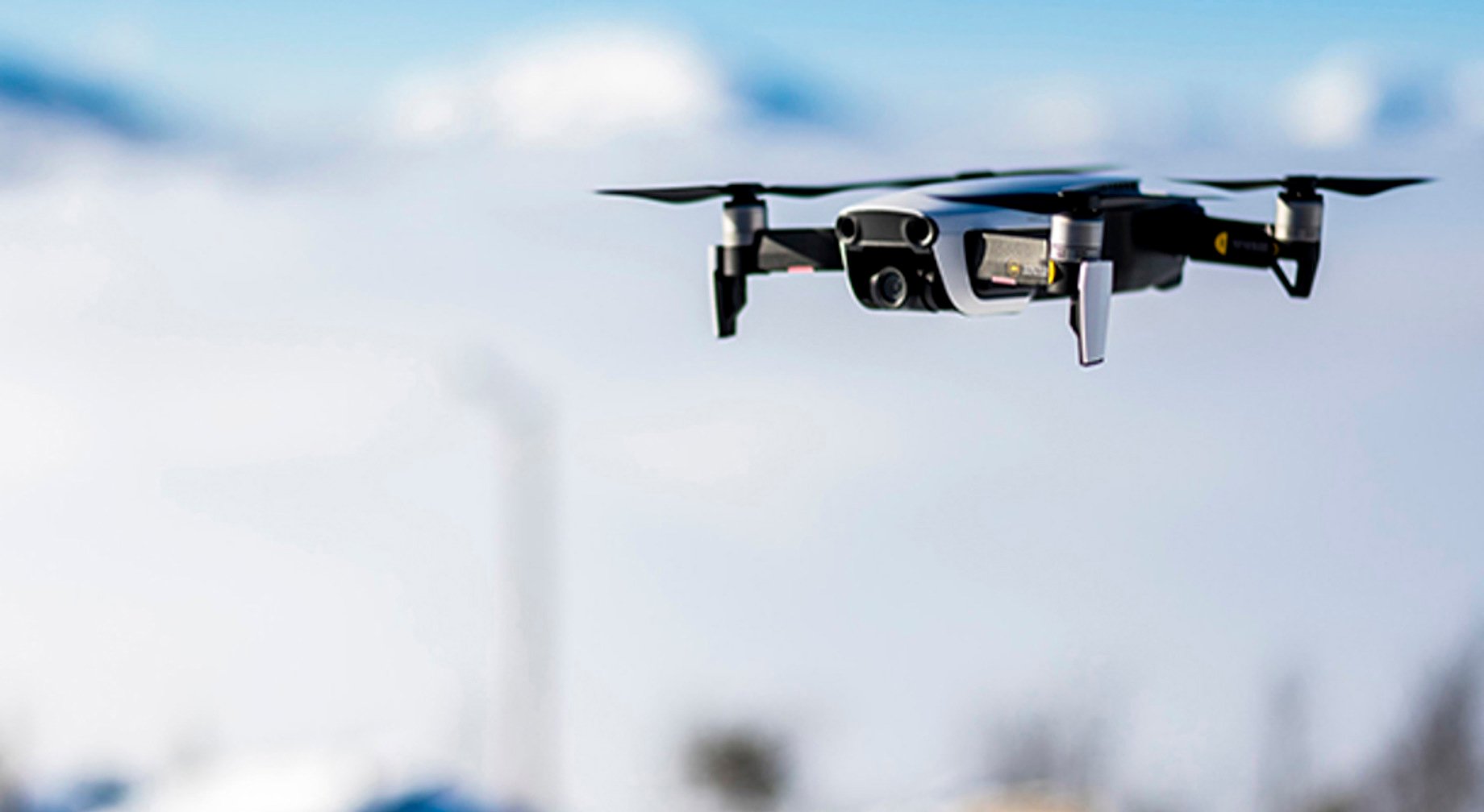 Drone som flyr i en klar blå himmel med snødekte fjell i bakgrunnen